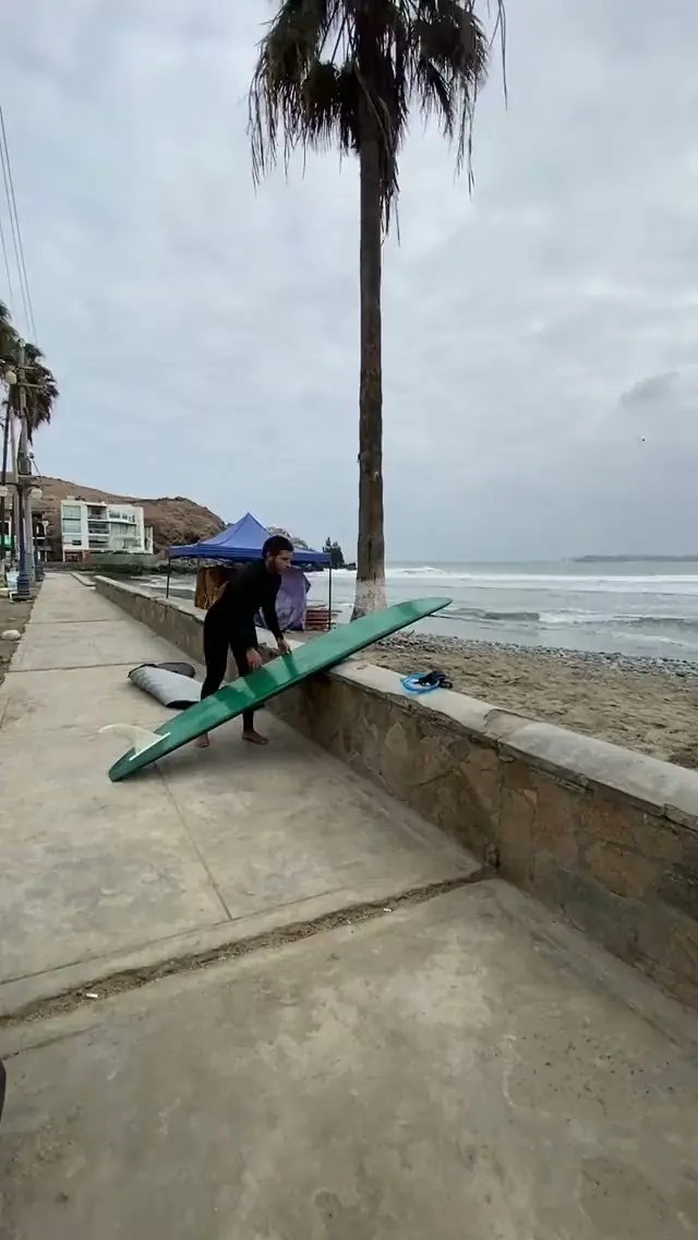 Surfista camina por la orilla de Playa Makaha con su tabla y un vaso de Fiera